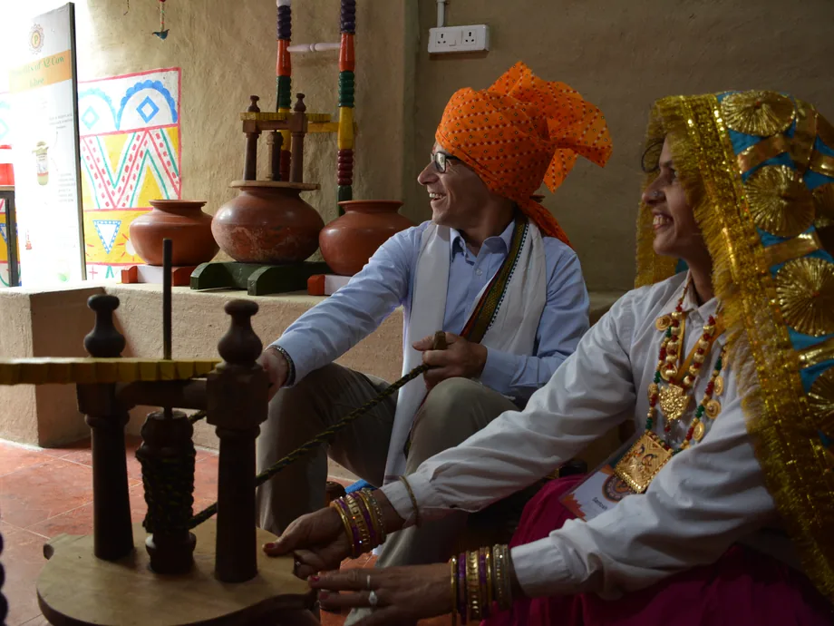 A man in an orange turban and a woman in a gold-bordered dupatta seated at a wooden bilona